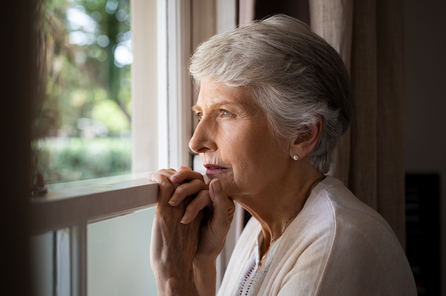 Sad woman with Lyme disease and lewy body dementia looking out the window.